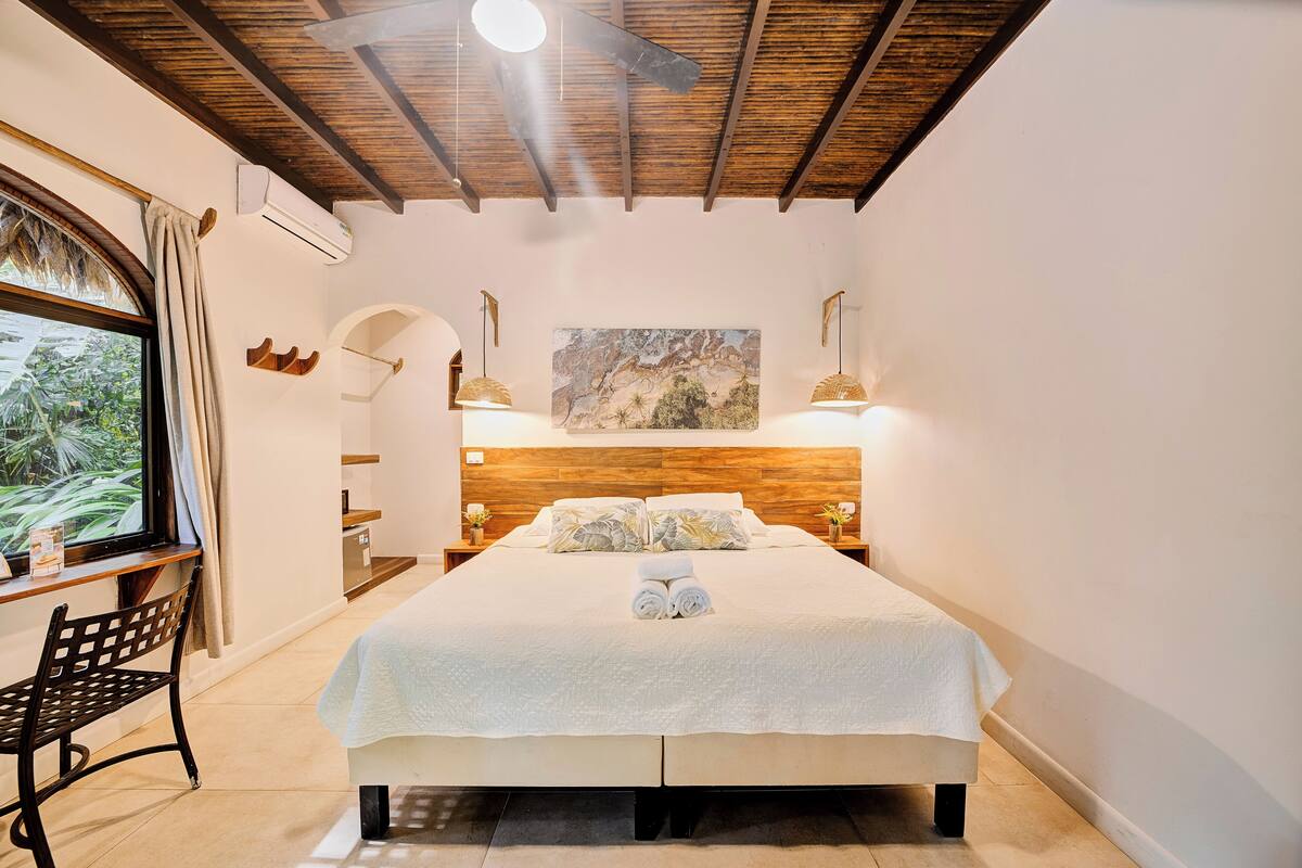 A bedroom with a bed, a desk, a chair, a window, and a painting on the wall.