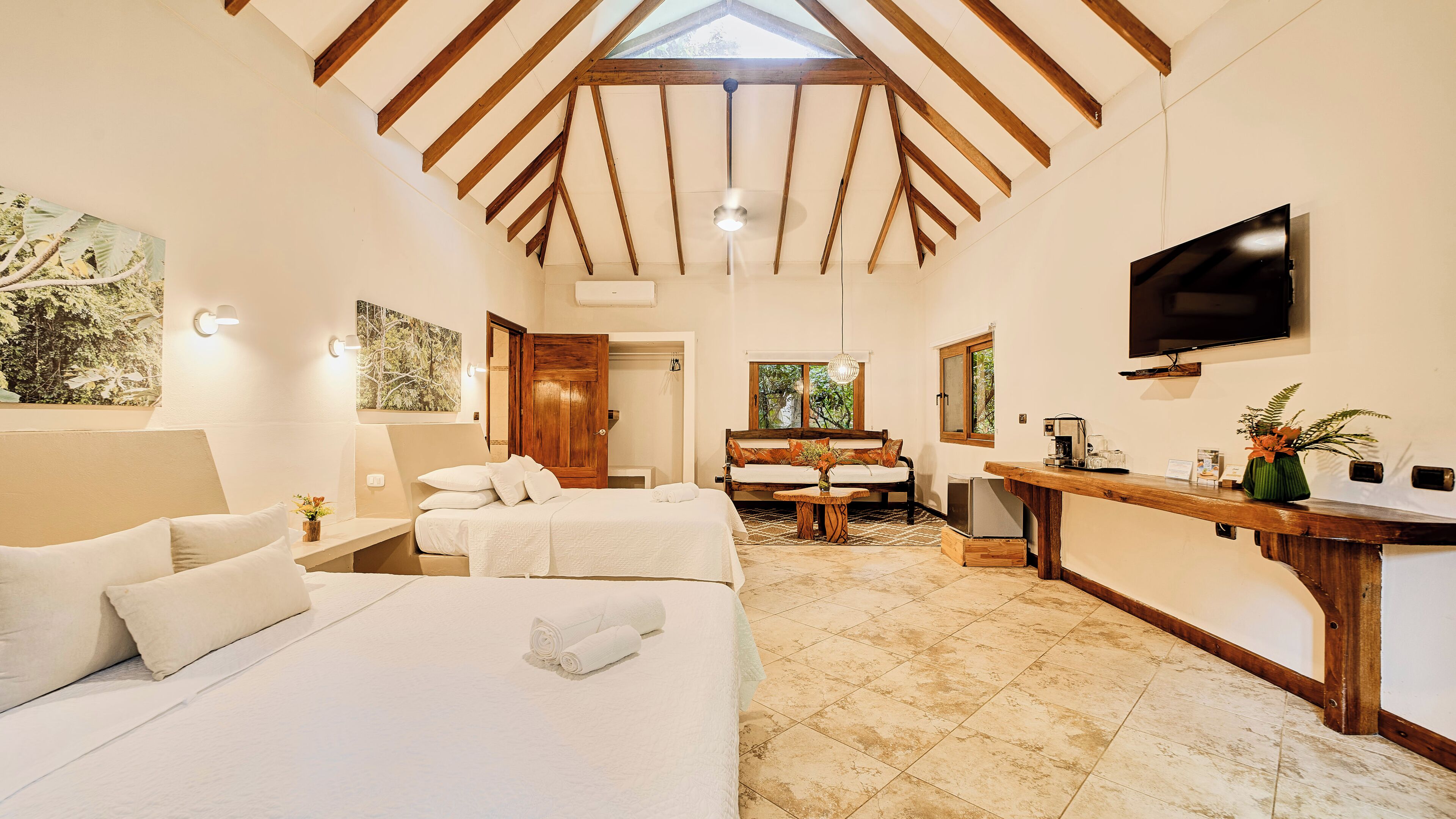 Un dormitorio con dos camas, techo de madera, televisor y ventana con vistas.
