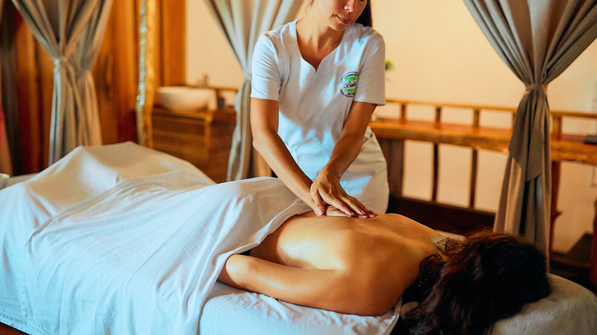 A massage therapy session in a room with wooden furniture and curtains.