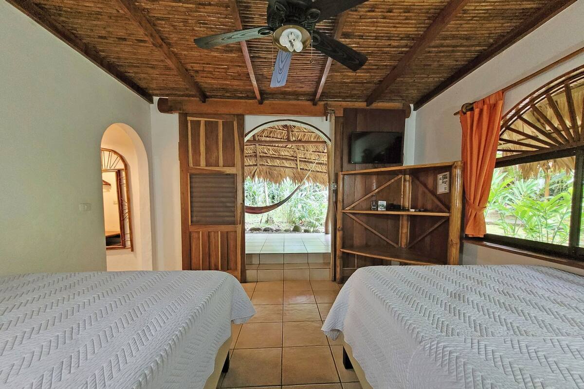 A room with two beds, a ceiling fan, a TV, and a view of the outdoors.