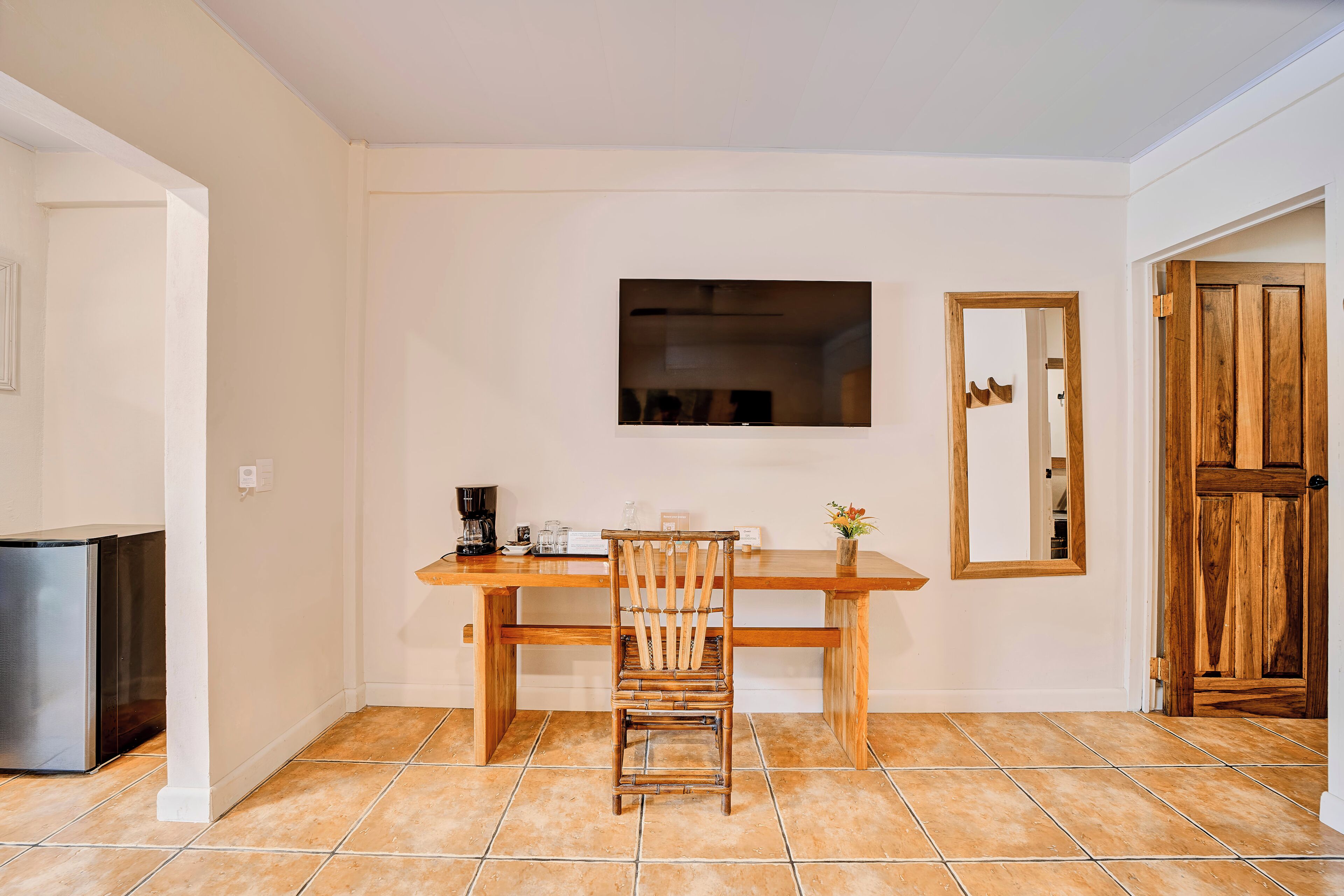 A dining area with a wooden table, a chair, a TV mounted on the wall, and a wooden door.