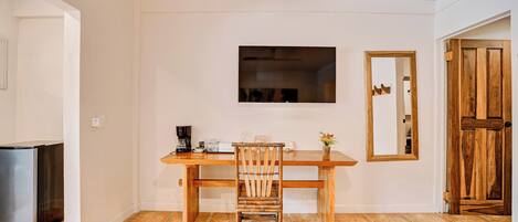 Un comedor con una mesa de madera, una silla, un televisor montado en la pared y una puerta de madera.