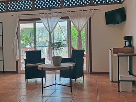 Una habitación con una mesa redonda, dos sillas, una planta en maceta, un televisor montado en la pared y una cafetera en un estante.