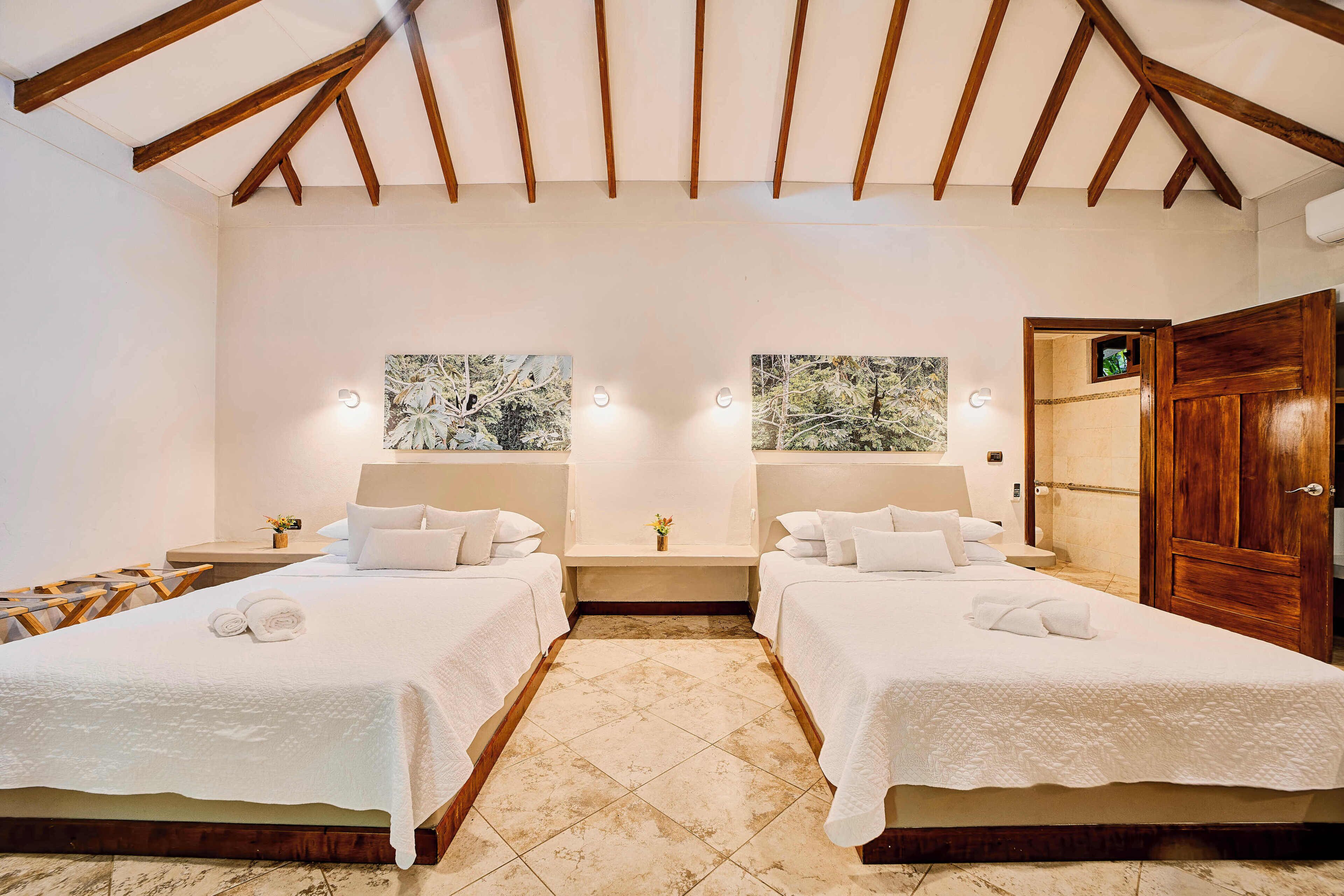 Une chambre d’hôtel avec deux lits, un plafond en bois et des œuvres d’art accrochées aux murs.