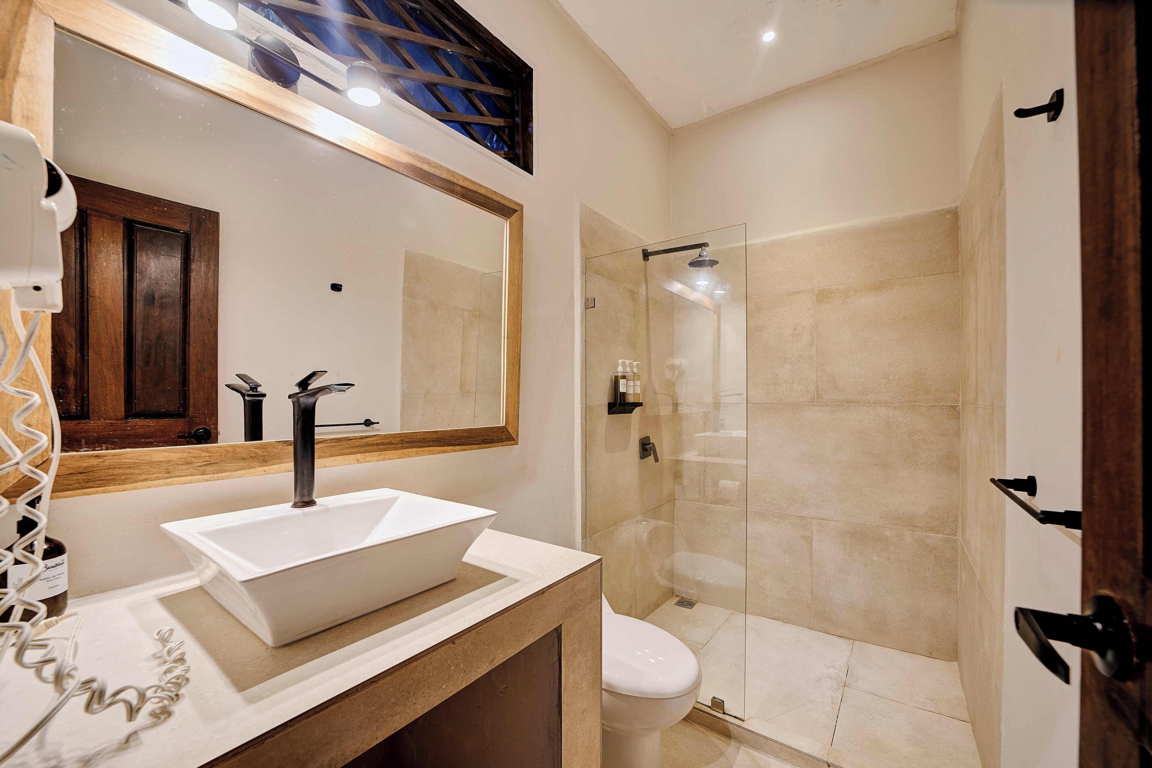 A bathroom with a white sink, a large mirror, a glass shower enclosure, and a wooden door.