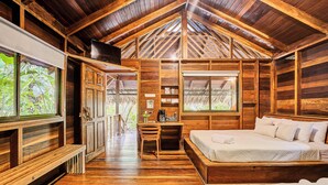 A wooden cabin interior with a lofted ceiling, a bed, a desk, and a television. - Cariblue Beach and Jungle Resort (Cahuita)