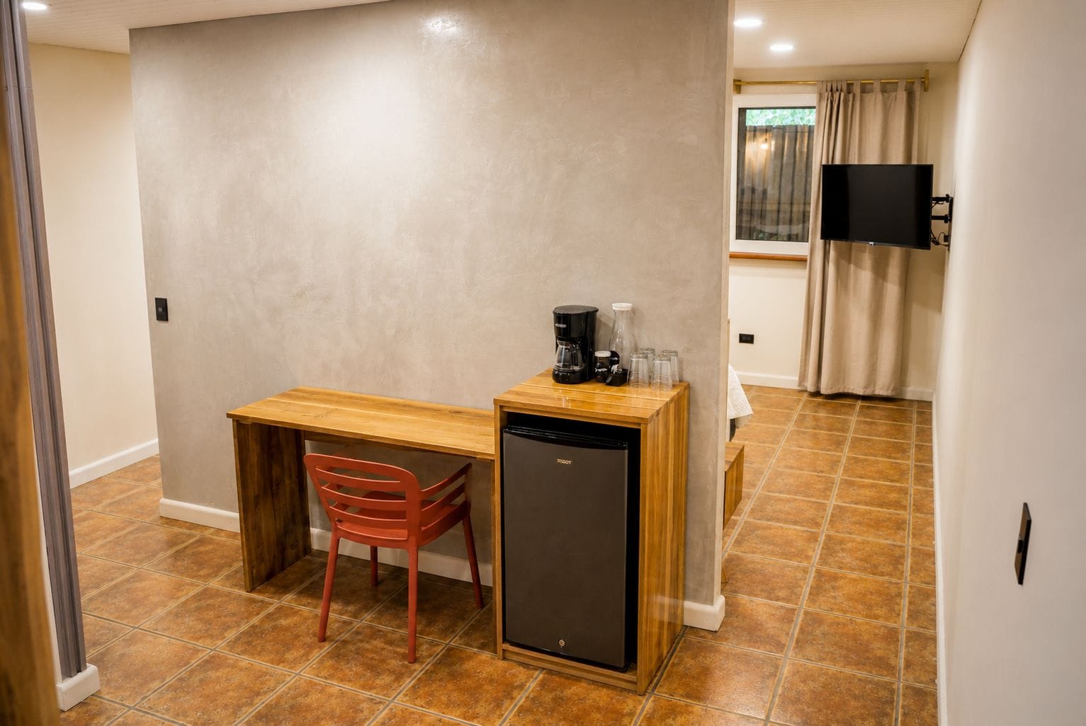 A compact kitchenette with a wooden countertop, a red chair, a black refrigerator, and a coffee maker.