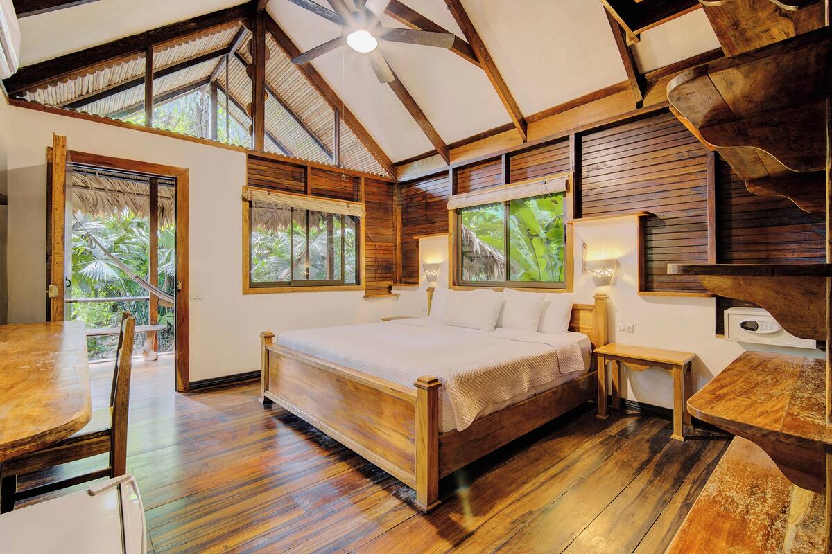 A spacious bedroom with a large bed, wooden flooring, and a ceiling fan.