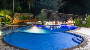 A nighttime swimming pool area with multiple pools, surrounded by trees and a thatched-roof structure. - Cariblue Beach and Jungle Resort (Cahuita)