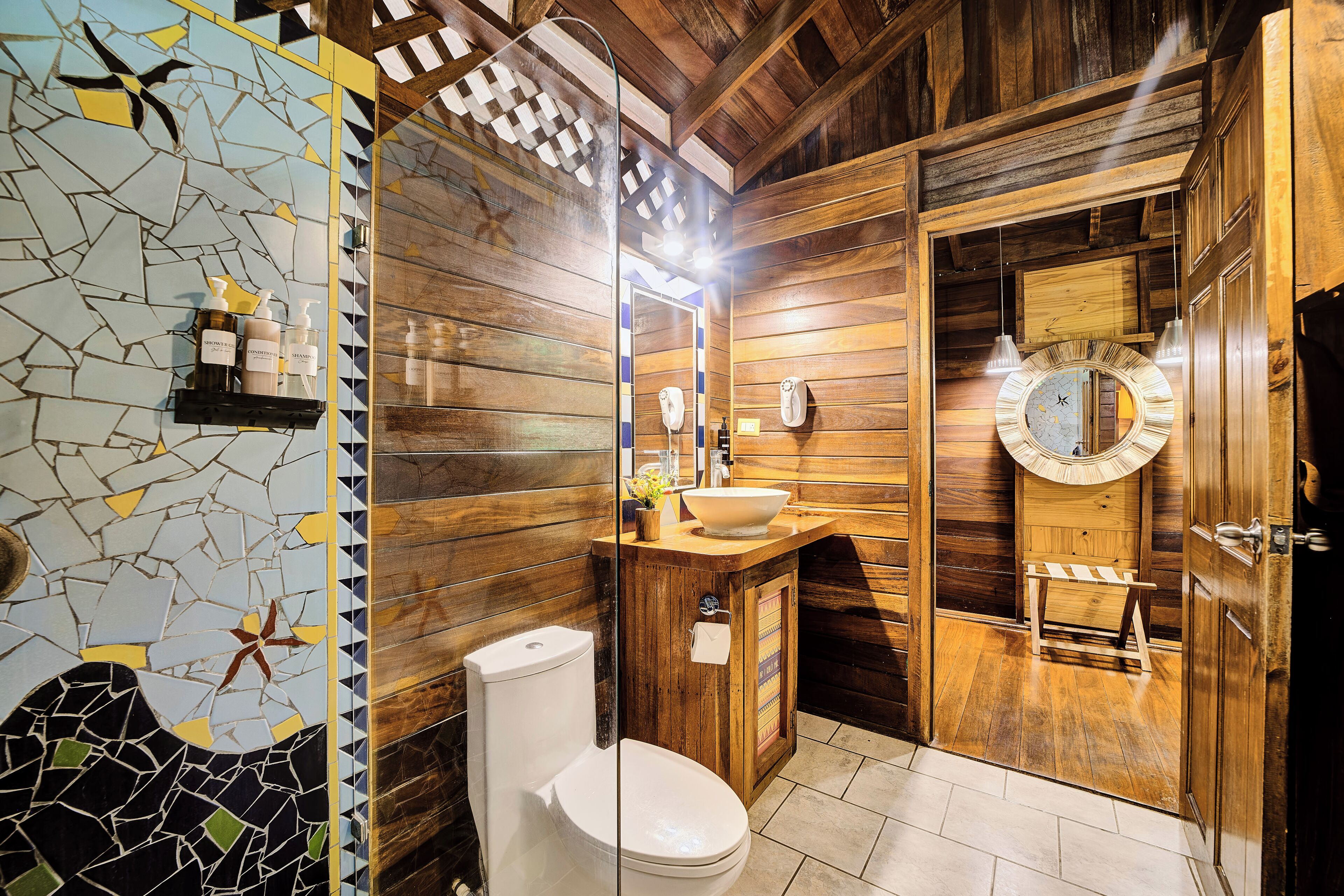 Une salle de bain en bois avec un mur décoré de mosaïques, un lavabo, des toilettes et un miroir.