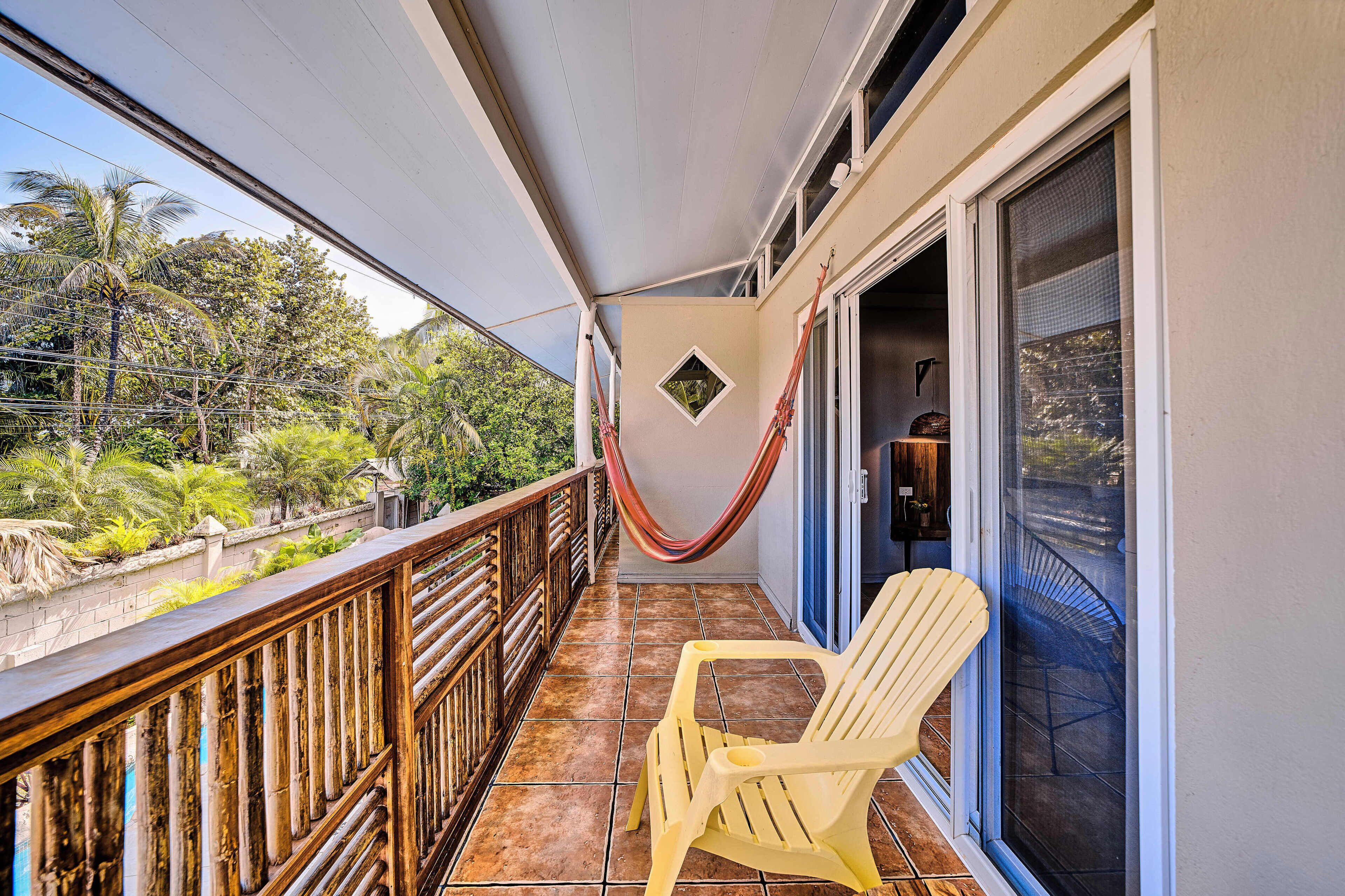A balcony with a hammock, a chair, and a view of greenery.