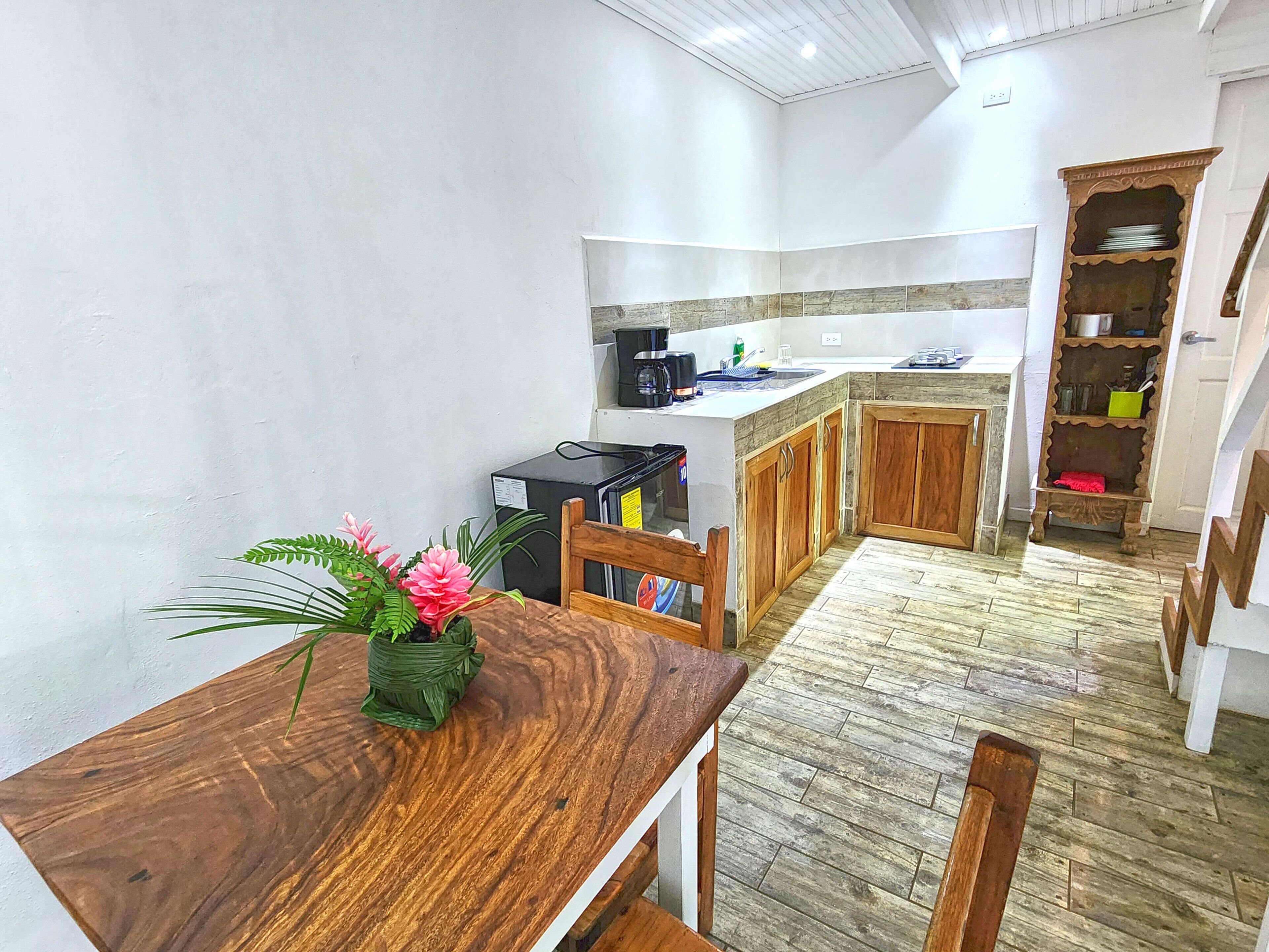 A compact kitchen with wooden cabinets, a dining table with a vase of flowers, and a staircase leading to another level.