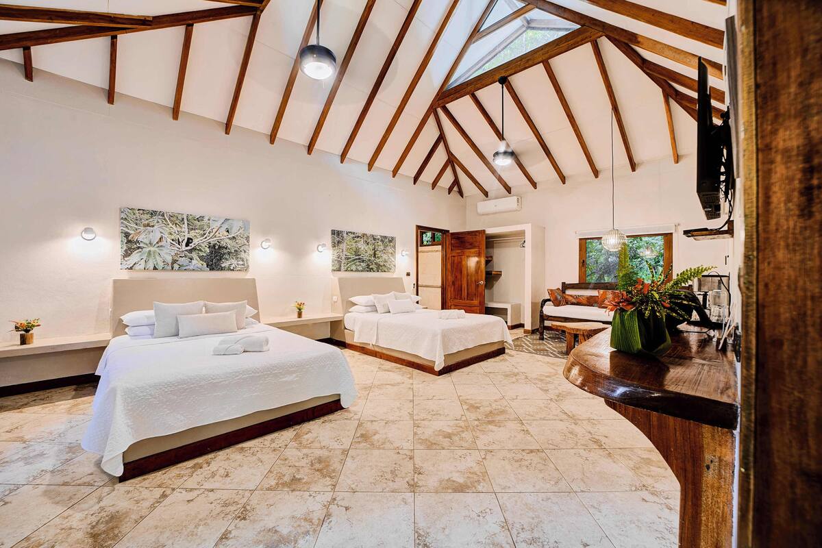 A spacious bedroom with two beds, a wooden ceiling, and a large window.