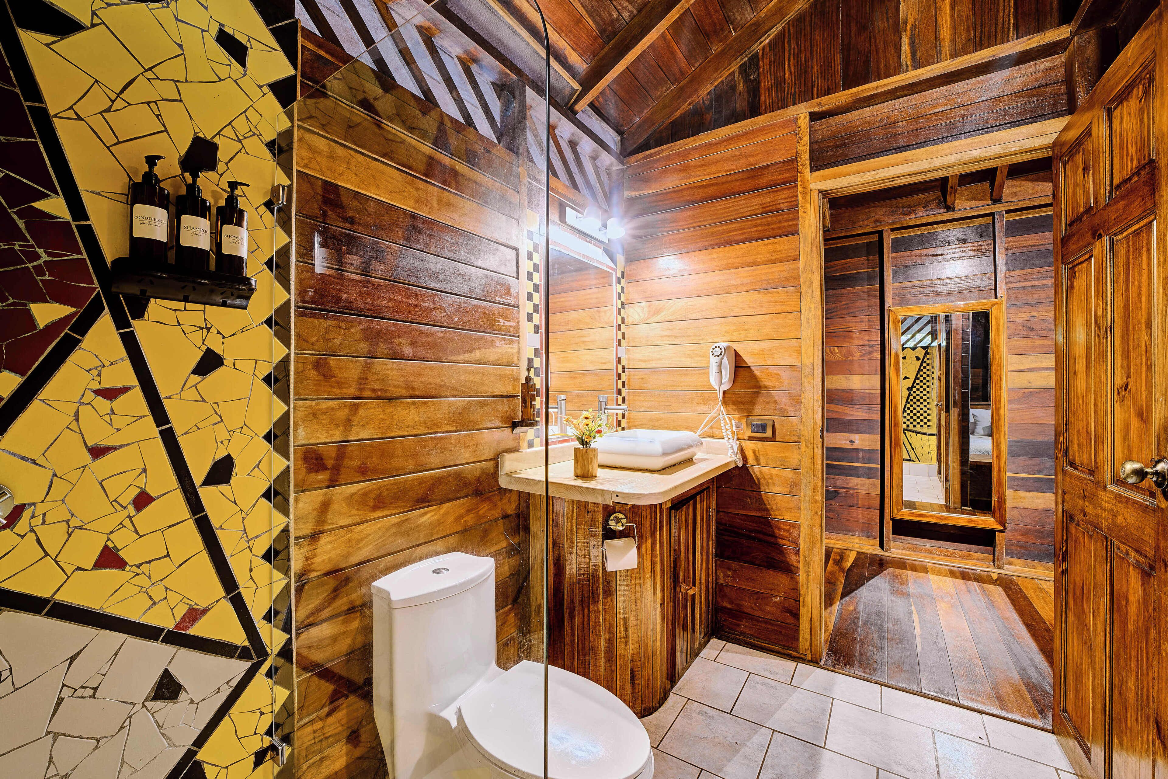 A wooden bathroom with a toilet, sink, and mirror.