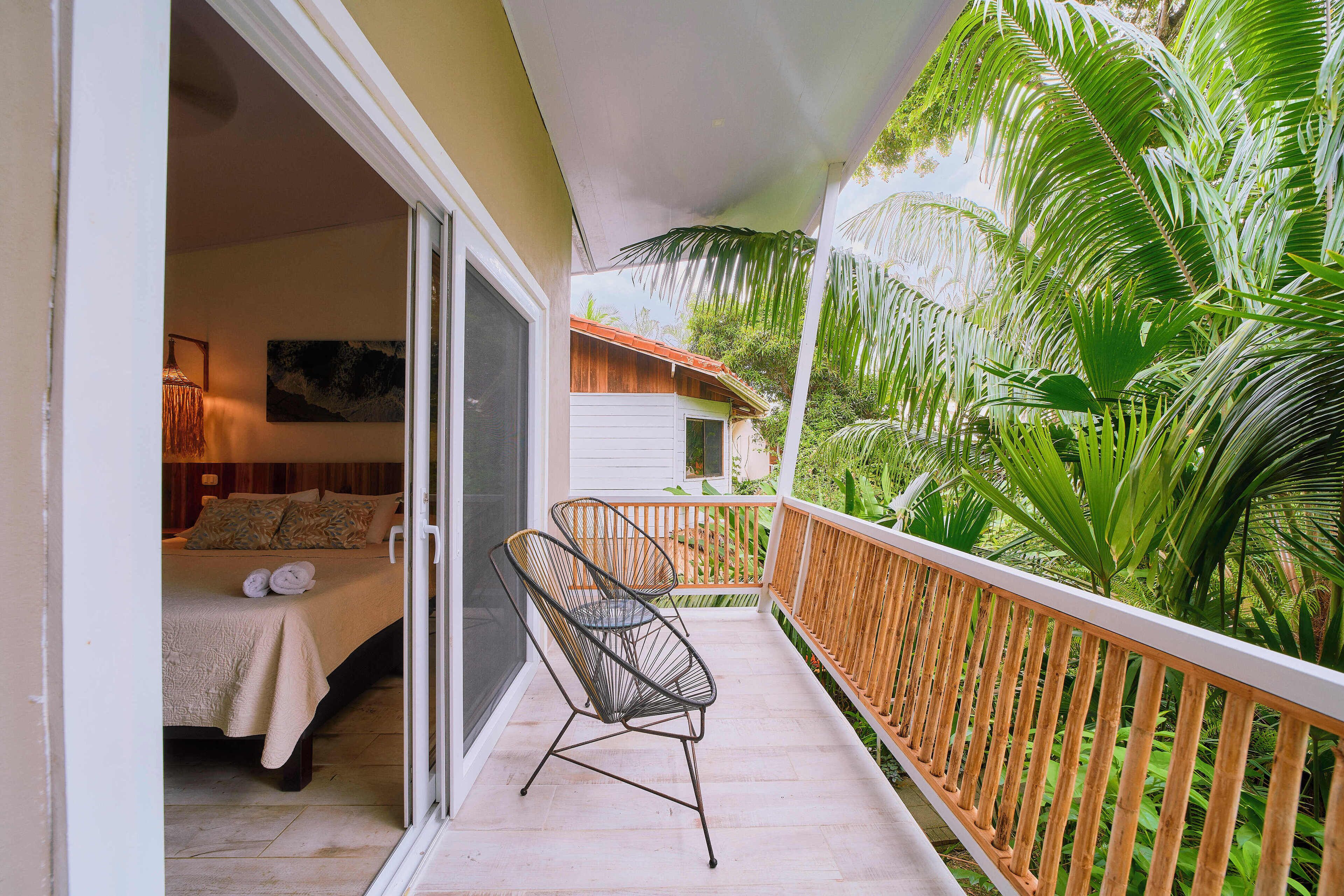 A balcony with a bed, a chair, and lush greenery.