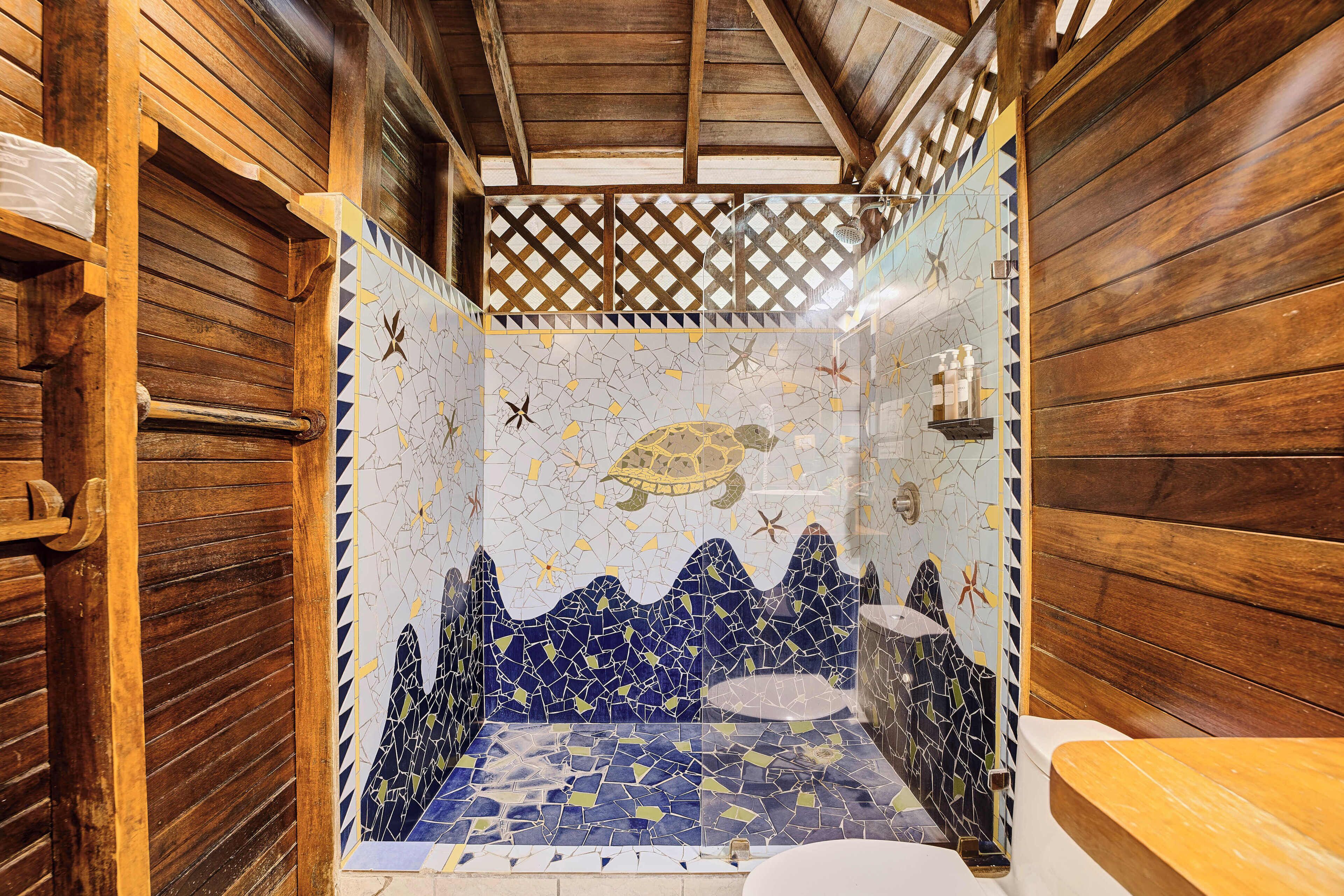 A bathroom with wooden walls, a mosaic shower wall, and a wooden bench.