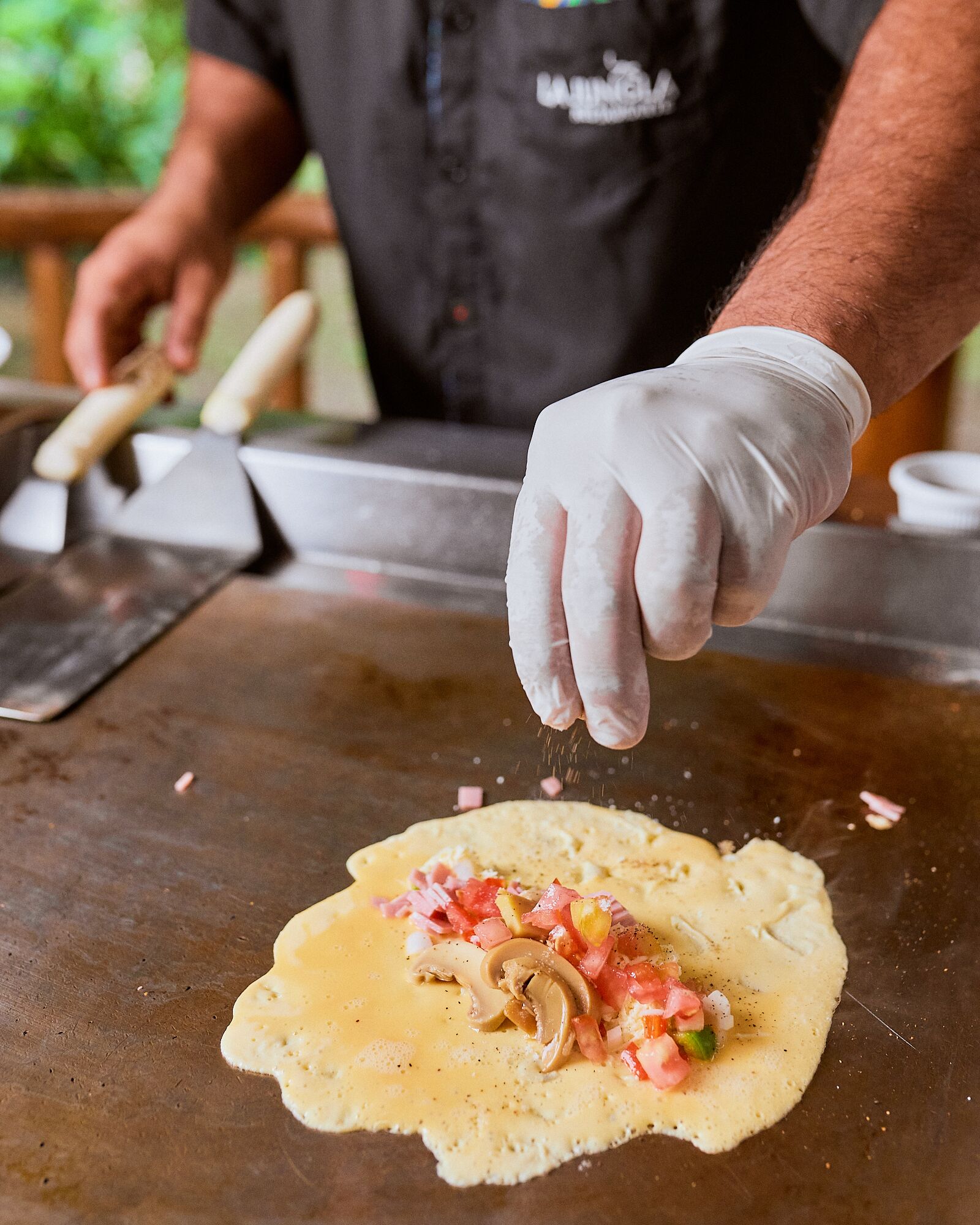A person preparing a dish on a flat cooking surface, wearing gloves, and using a spatula.