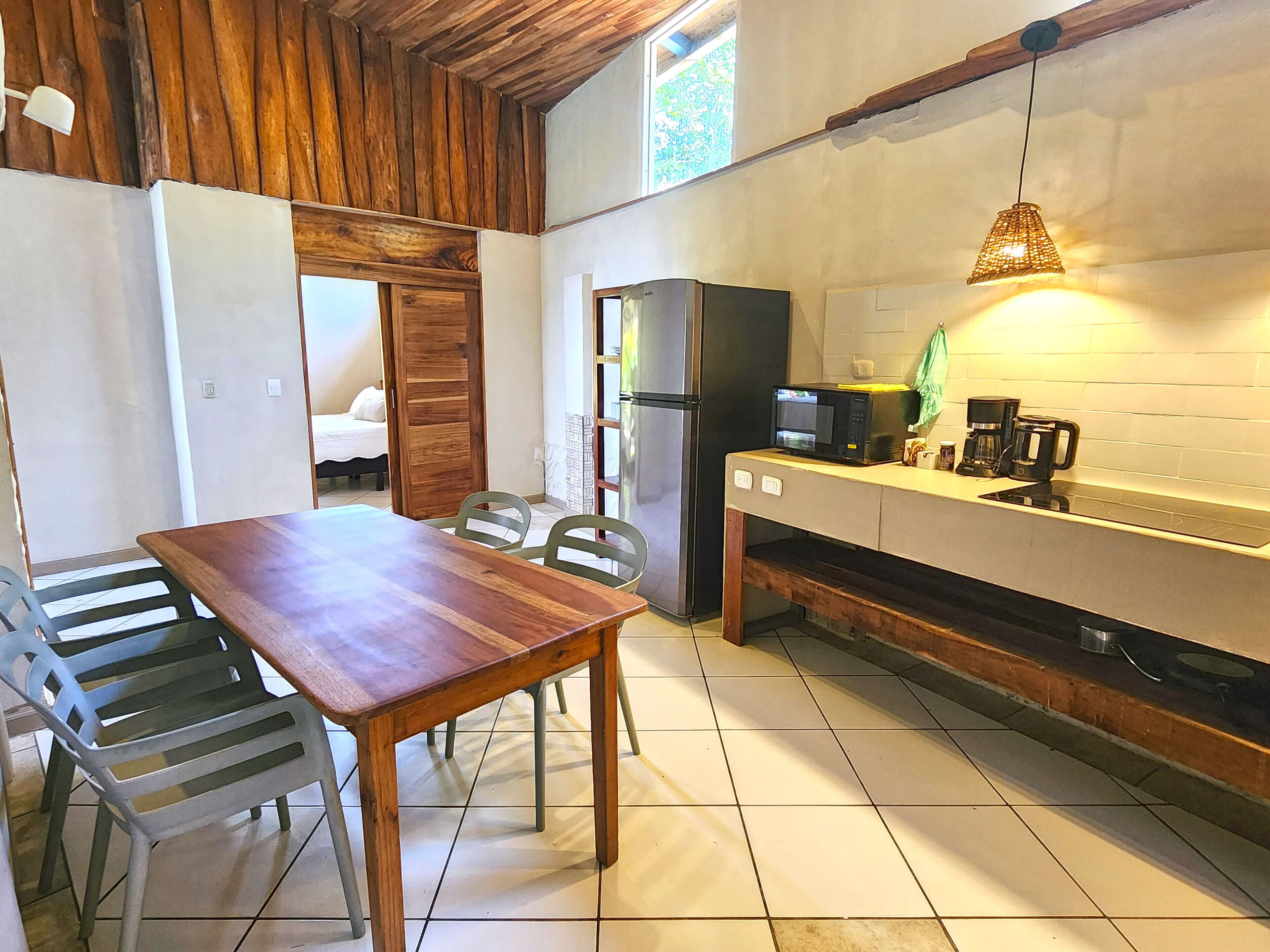 A compact kitchen with a wooden table and chairs, a refrigerator, a microwave, and a coffee maker.
