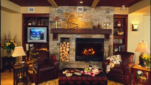 A cozy living room with a stone fireplace, leather sofas, a television, and a fireplace mantel with decorative items. - Sundance Resort (Beaverdell)