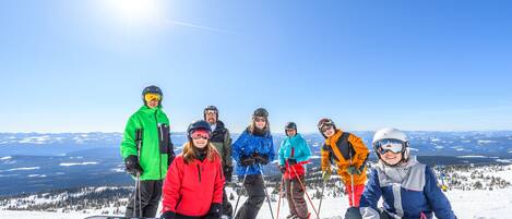 A group of people on a snowy mountain with ski equipment, standing and sitting on the snow.