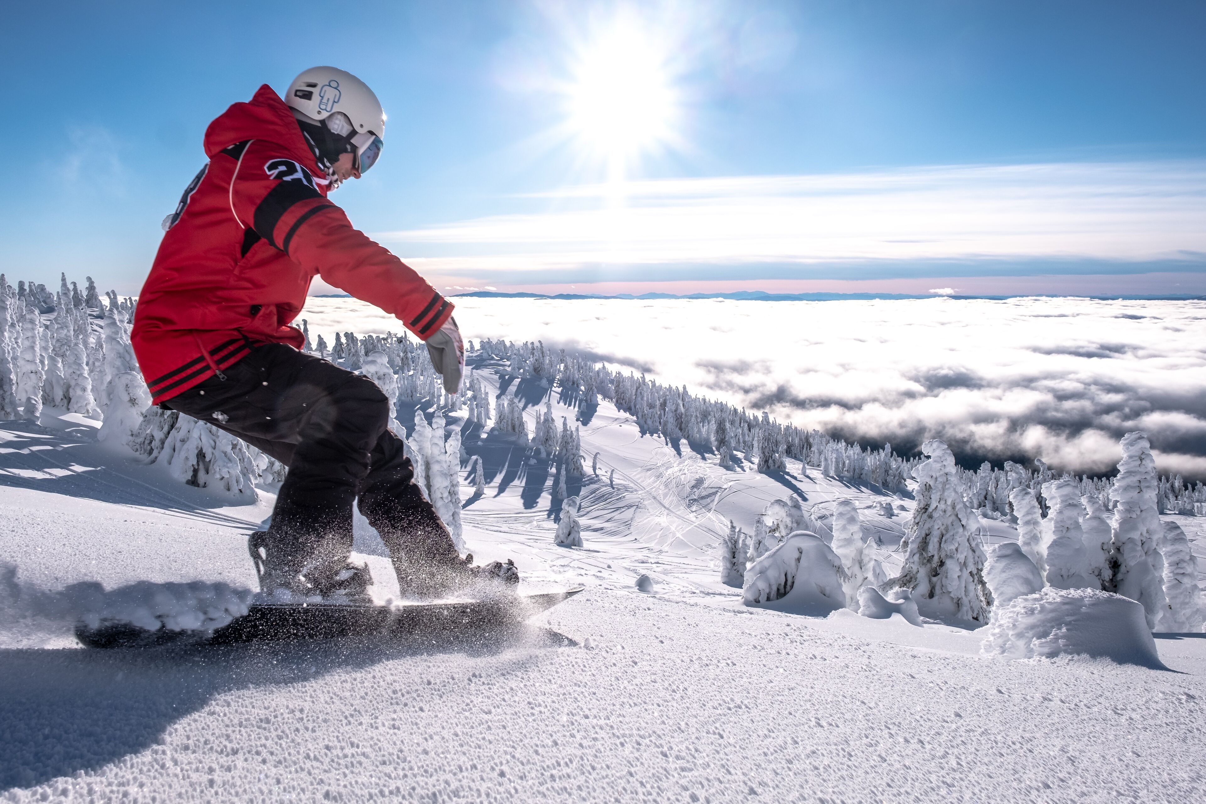 A person snowboarding on a snowy mountain with trees and a clear sky.