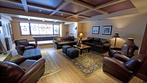 A spacious living room with leather sofas, a pool table, and a large window with a view of the pool. - Sundance Resort (Beaverdell)