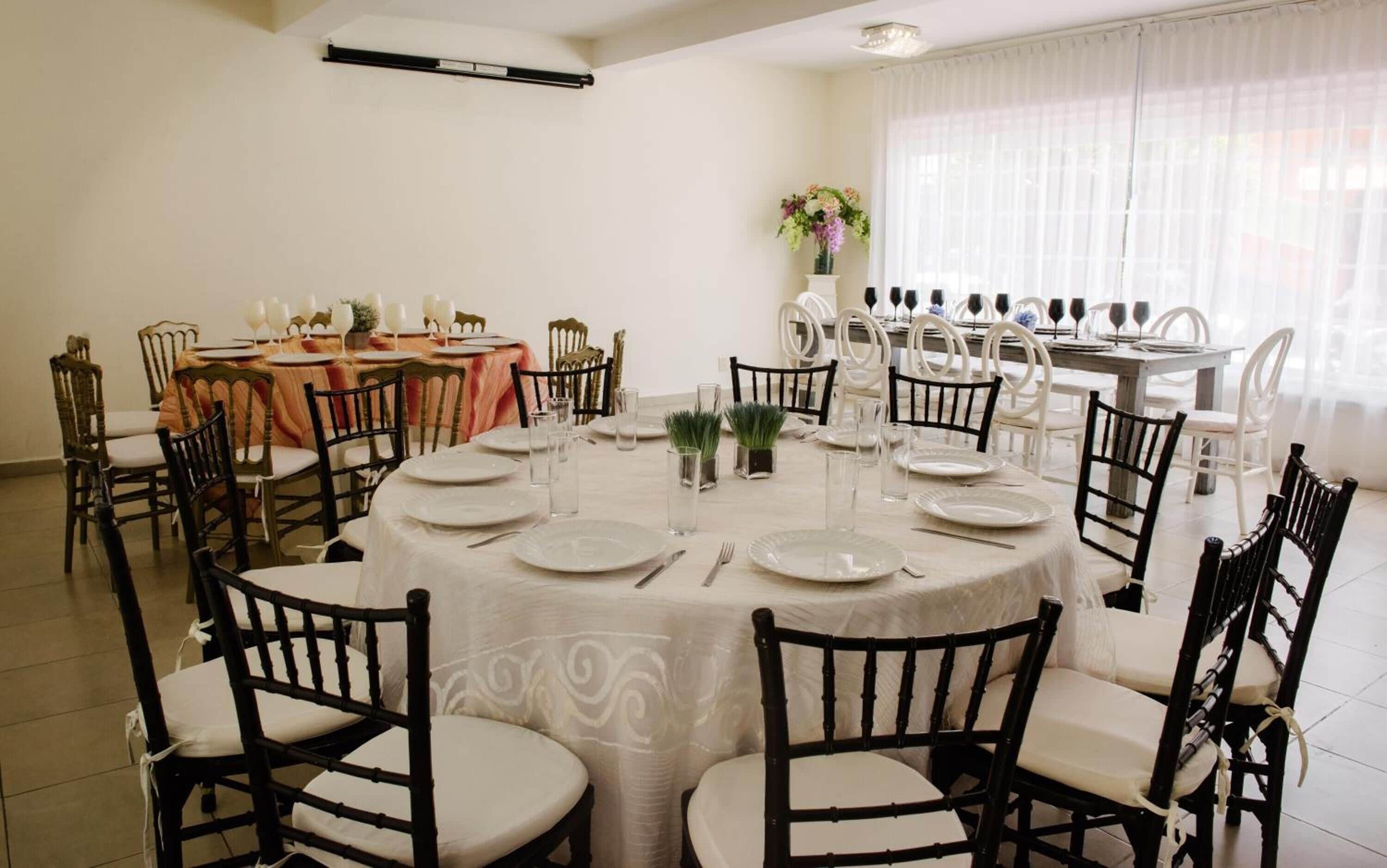 A dining area with round tables, chairs, and a large window with curtains.