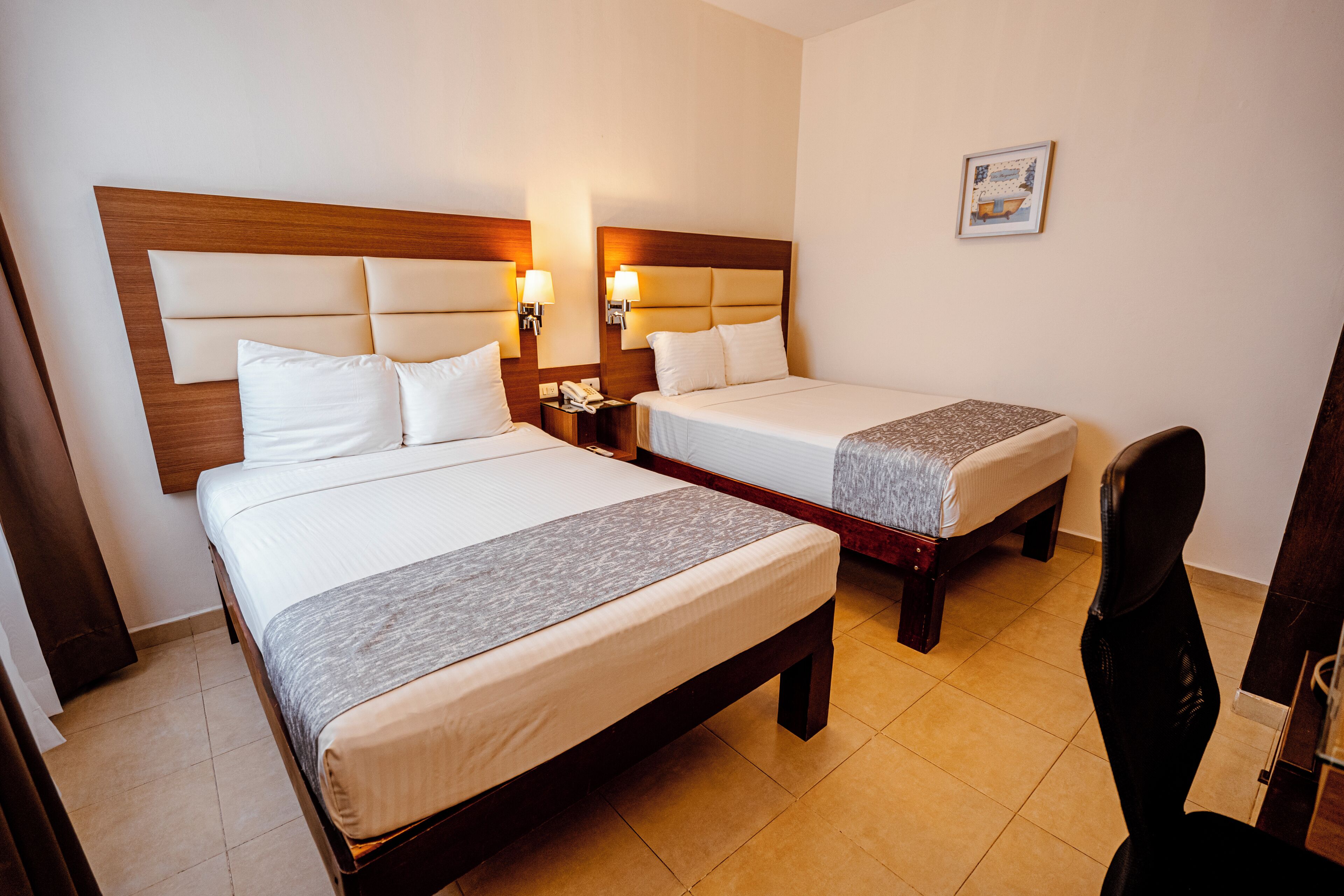 A hotel room with two beds, wooden headboards, bedside lamps, a desk, and a chair.