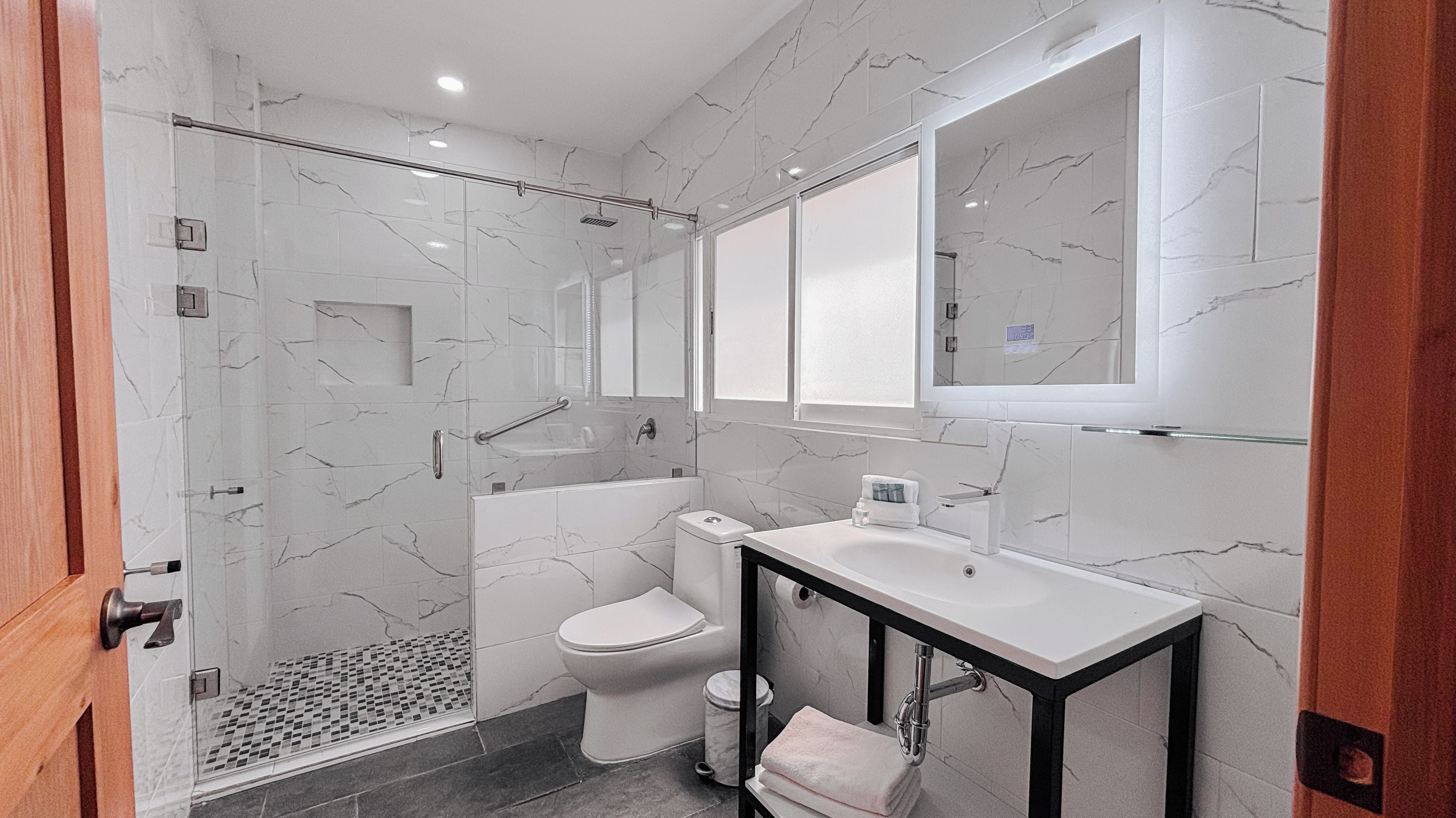 Un baño moderno con ducha envuelta en vidrio, inodoro y tocador con lavamanos.