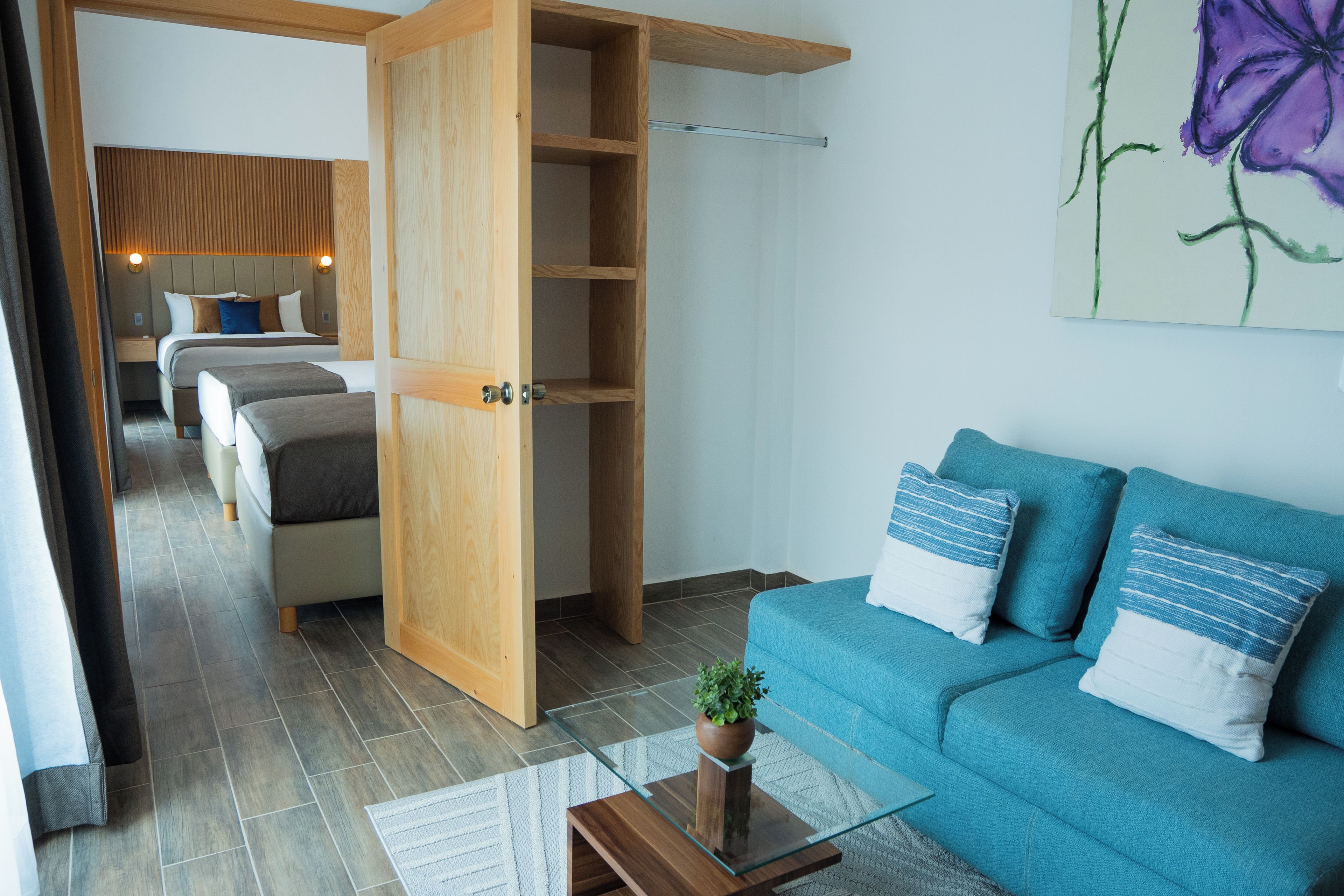 Quarto de hotel moderno com uma cama, um sofá, uma mesa de centro de vidro e um guarda-roupa de madeira.