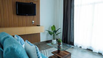 Una sala de estar moderna con un televisor de pantalla plana montado en una pared de madera, una mesa de centro de vidrio con una planta, y un sofá azul.