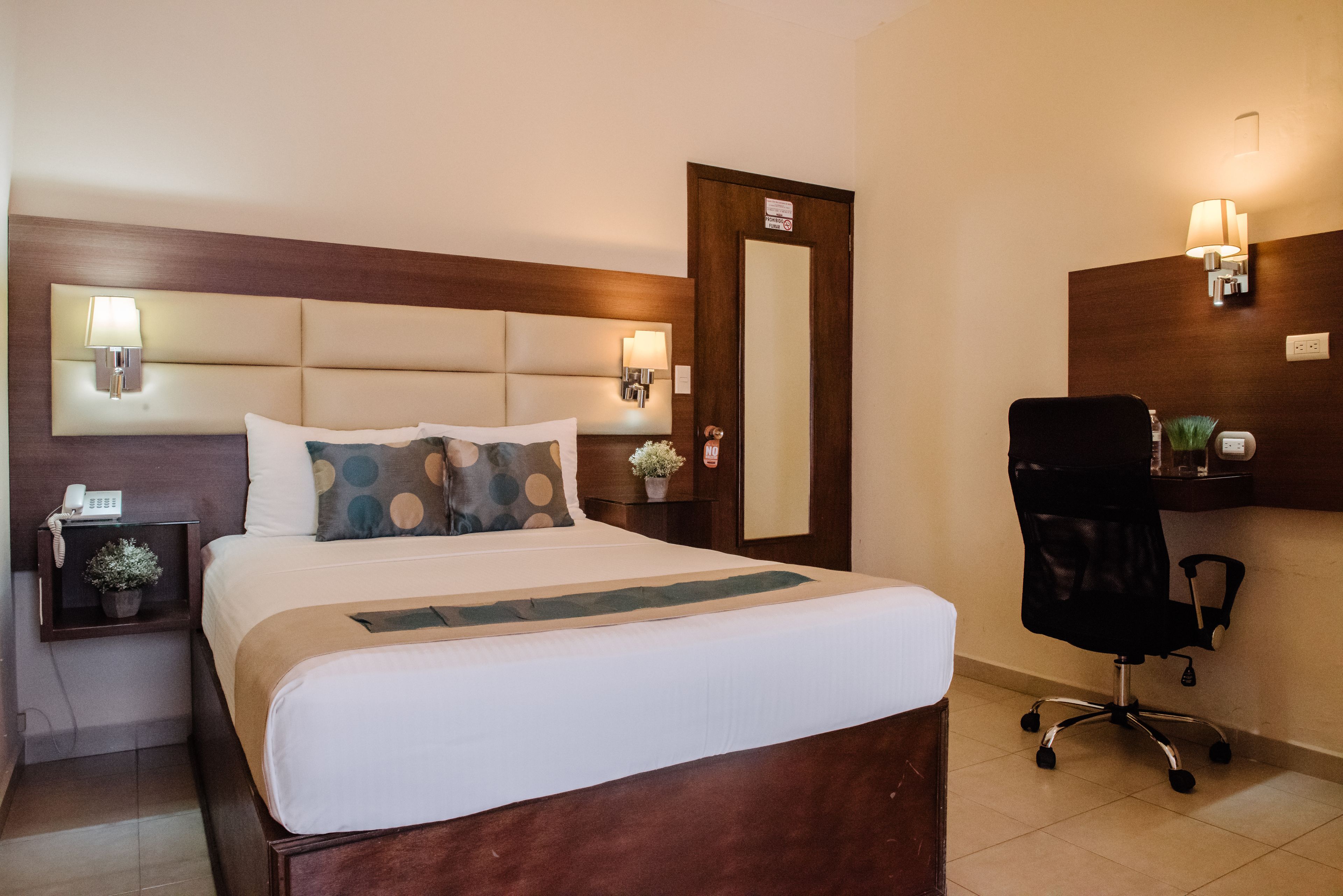 Quarto de hotel com uma cama grande, luminárias de cabeceira, uma escrivaninha com cadeira e um espelho.