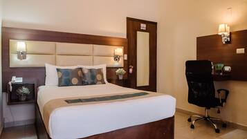 Quarto de hotel com uma cama grande, luminárias de cabeceira, uma escrivaninha com cadeira e um espelho.