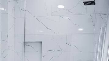 A modern bathroom with a marble backsplash, a bathtub, and a shower area.
