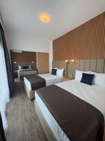 Habitación de hotel con dos camas, cabecero de madera, luz de techo y mesita de noche con lámpara.