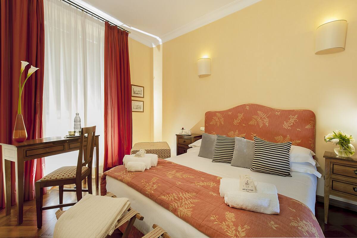 Una habitación de hotel con cama, escritorio, silla y mesita de noche.