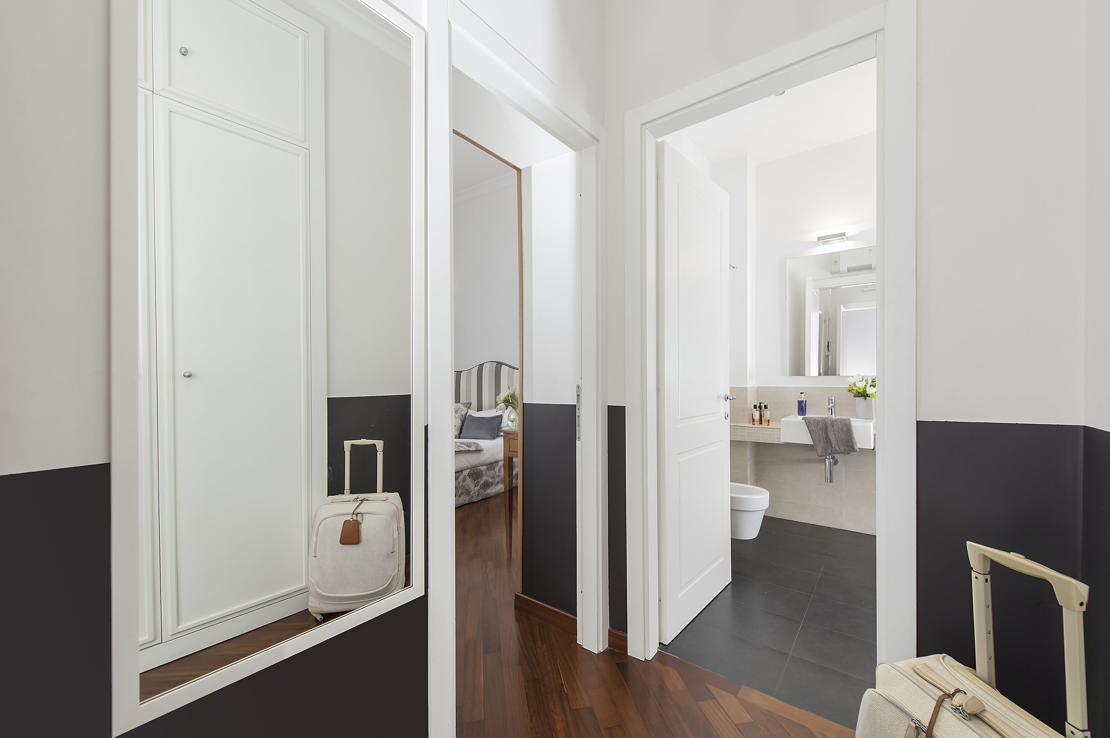 A hotel corridor with a bed, bathroom, and a suitcase.