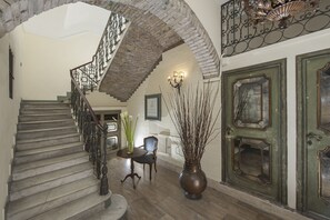 A grand staircase with a wrought iron railing, a dining area with a table and chairs, and a large vase with branches. - All’Orologio (Rome)