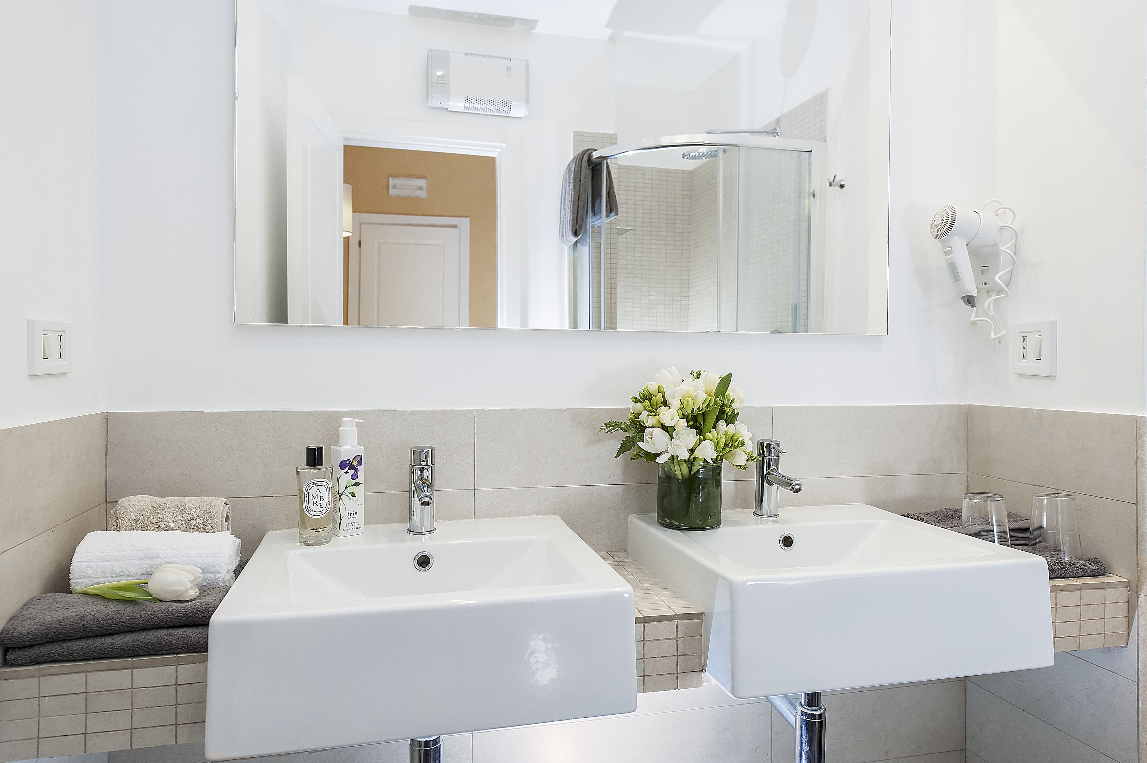 A modern bathroom with two sinks, a large mirror, a towel rack, and a shower area.
