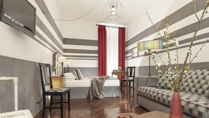 Ein modernes Hotelzimmer mit gestreiftem Wanddesign, einer Couch, einem Bett, einem Fernseher und einer Vase mit Blumen.