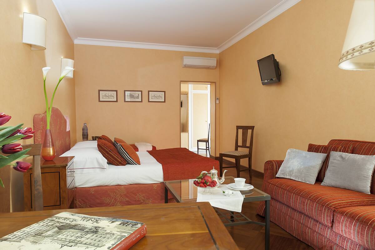 Una habitación de hotel con cama, sofá, una mesa con tetera y tazas, y una silla.