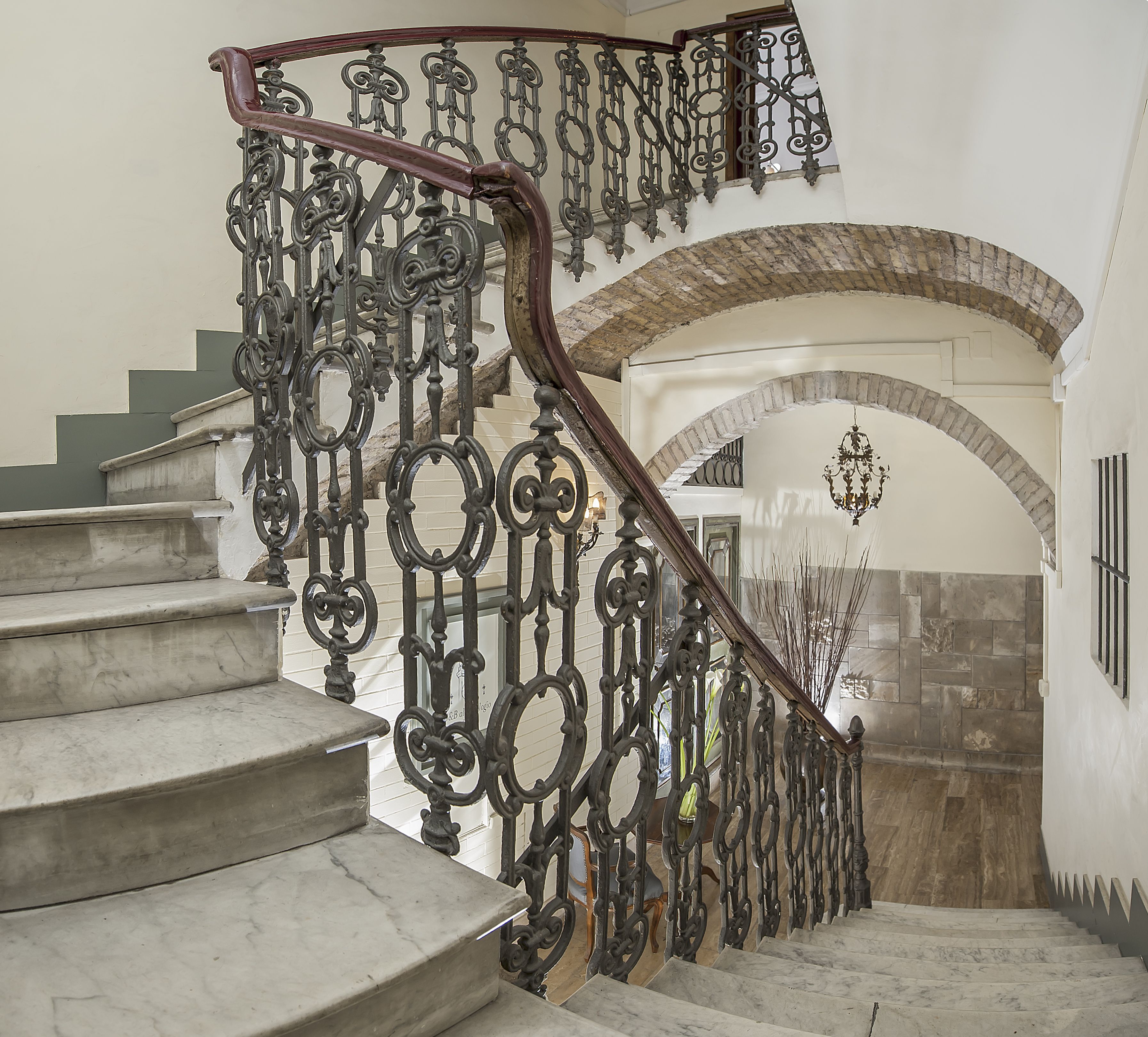 Una escalera con barandales de metal ornamentados y un muro de piedra con un arco.