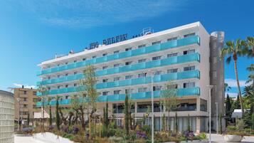 Un hôtel à plusieurs étages doté de balcons, d’un jardin aménagé et surplombant un ciel d’un bleu limpide.