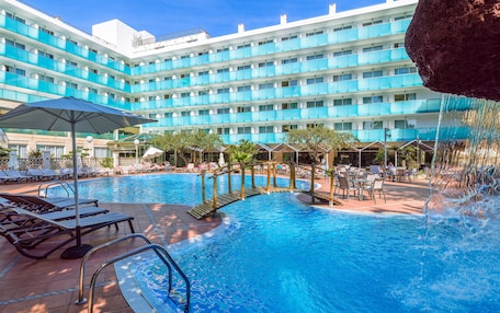 A hotel with a large pool area, multiple lounge chairs, and a waterfall feature.