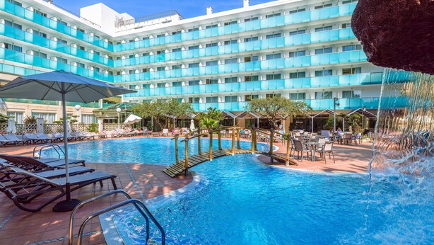 A hotel with a large pool area, multiple lounge chairs, and a waterfall feature. - H10 Delfín - Adults Only (Salou)