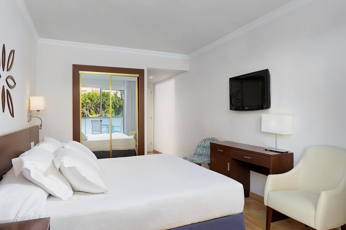 Habitación de hotel con cama, escritorio, silla, televisor y ventana con vistas a zonas verdes.