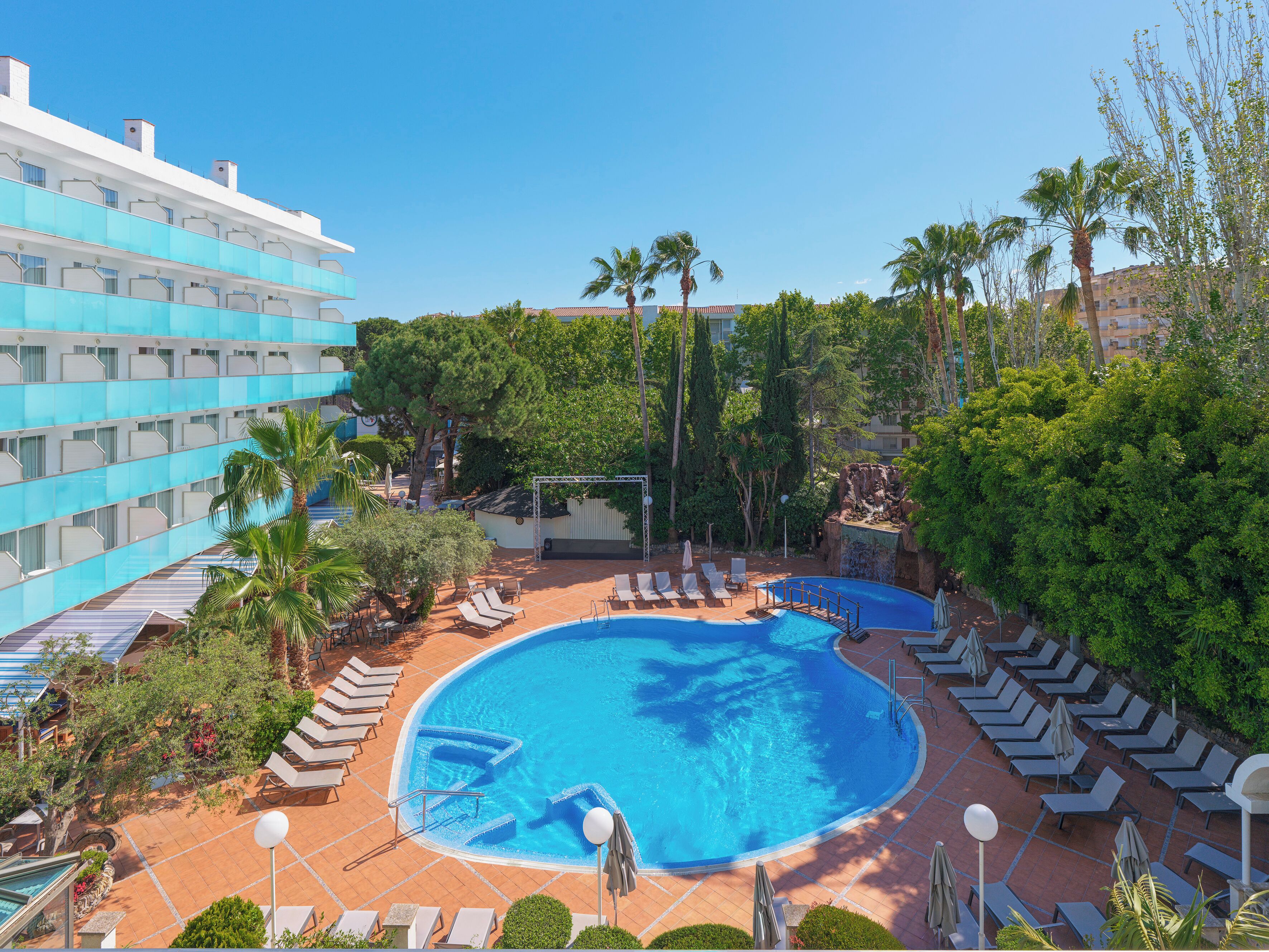 Un hotel con una amplia piscina, tumbonas y palmeras.