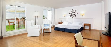 A hotel room with a bed, two chairs, a table, a TV, and a balcony with outdoor furniture.