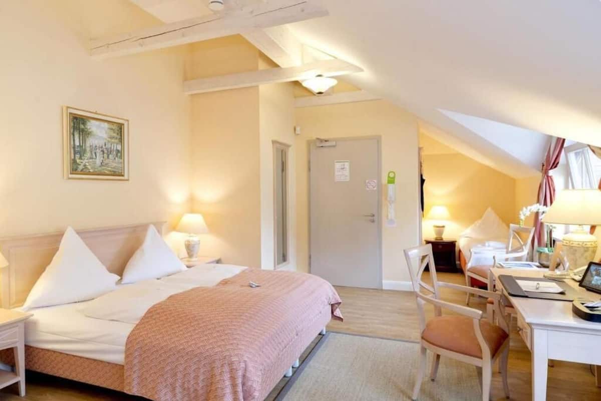 A hotel room with a bed, desk, chair, and a painting on the wall.