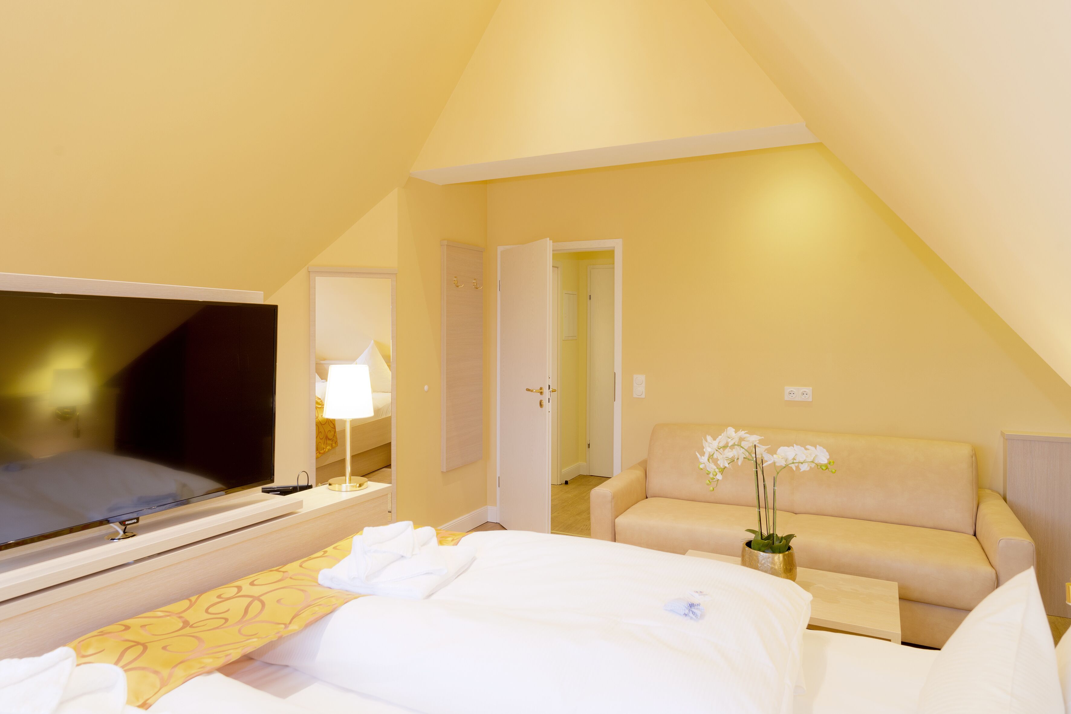 Ein Hotelzimmer mit einem Bett, einem Fernseher, einer Couch und einem kleinen Tisch mit einer Blumenvase.